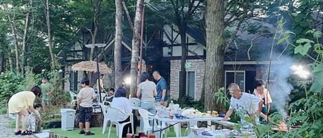 An outdoor dining area with tables and chairs, surrounded by trees and a building with stone walls.