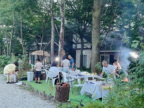 An outdoor dining area with tables and chairs, surrounded by trees and a building with stone walls. - Pension Balmy (Nasu)