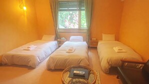 Una camera d'albergo con due letti singoli, un tavolino, una sedia e una finestra che si affaccia sul verde.