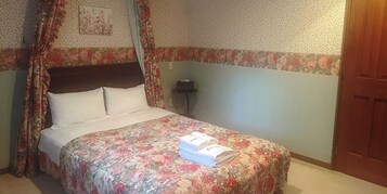 Una cama bien hecha con una colcha estampada con motivos florales y una toalla doblada encima.