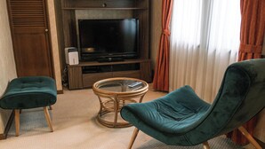 Una stanza con televisione, due poltrone, un tavolino e una sedia in vimini.