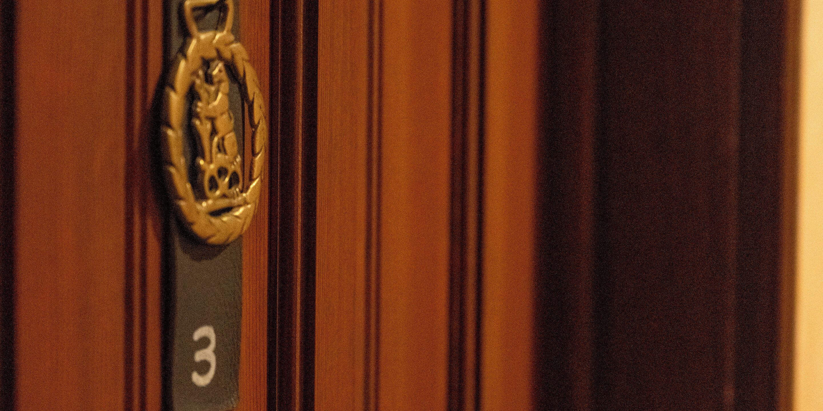 Primer plano de una puerta con picaporte de latón y placa con el número 3.