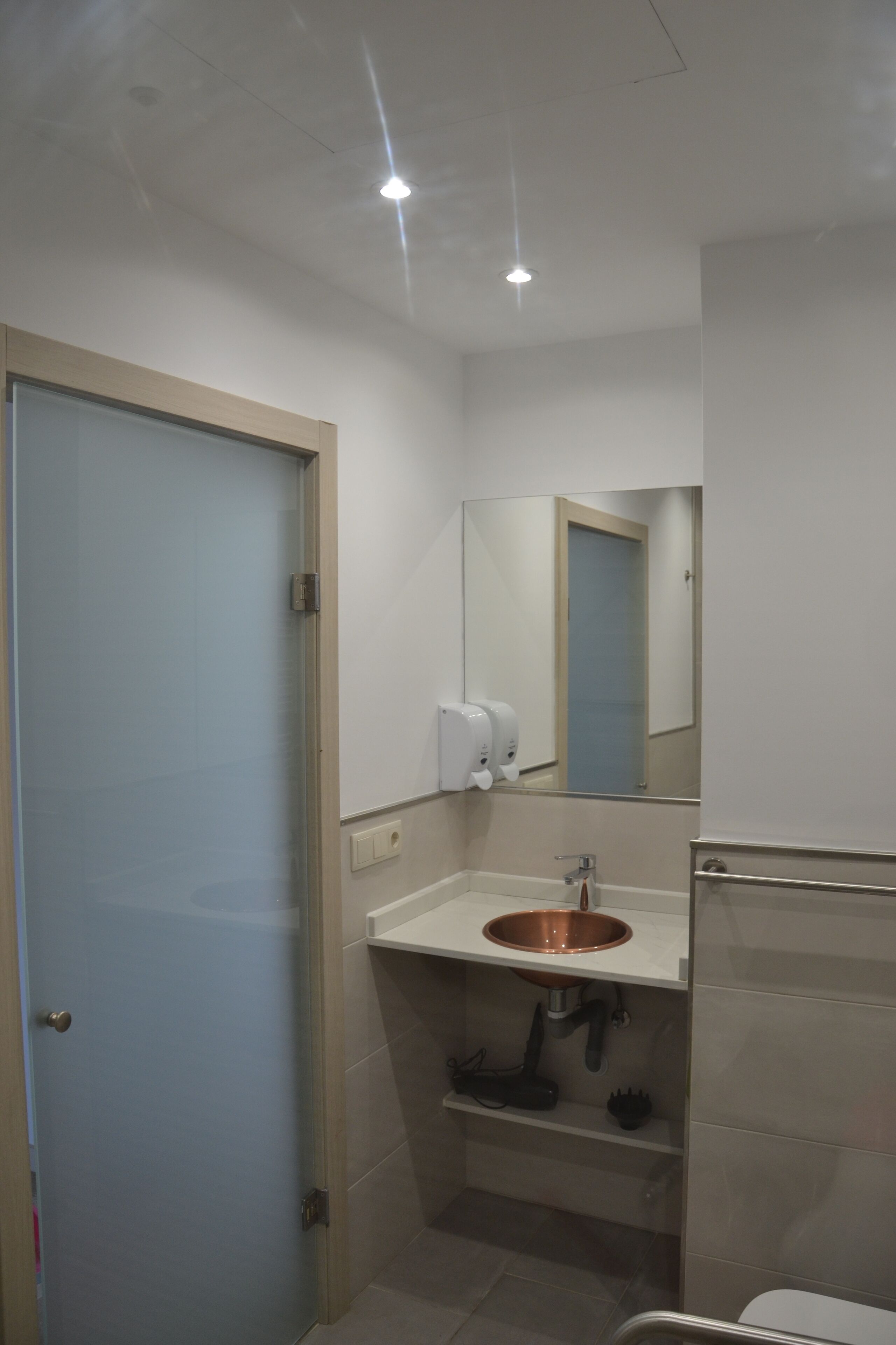 Un baño pequeño con lavamanos, espejo y secador de manos.