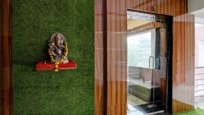 A room with a green artificial grass wall, a wooden door, and a statue on a red base.