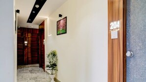 A hallway with a wooden door labeled 204, a potted plant, and a framed picture on the wall.