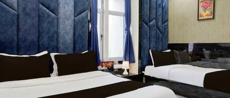 A hotel room with a large bed, a smaller bed, and a sofa. There is a window with curtains, a lamp, and a painting on the wall.