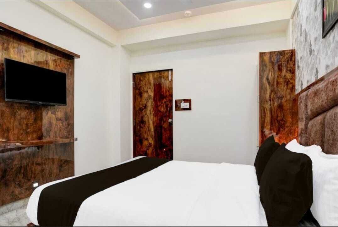 A hotel room with a large bed, a flat-screen TV mounted on the wall, and a wooden headboard.