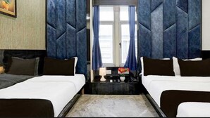 A hotel room with two beds, a nightstand, a lamp, and a window with curtains.