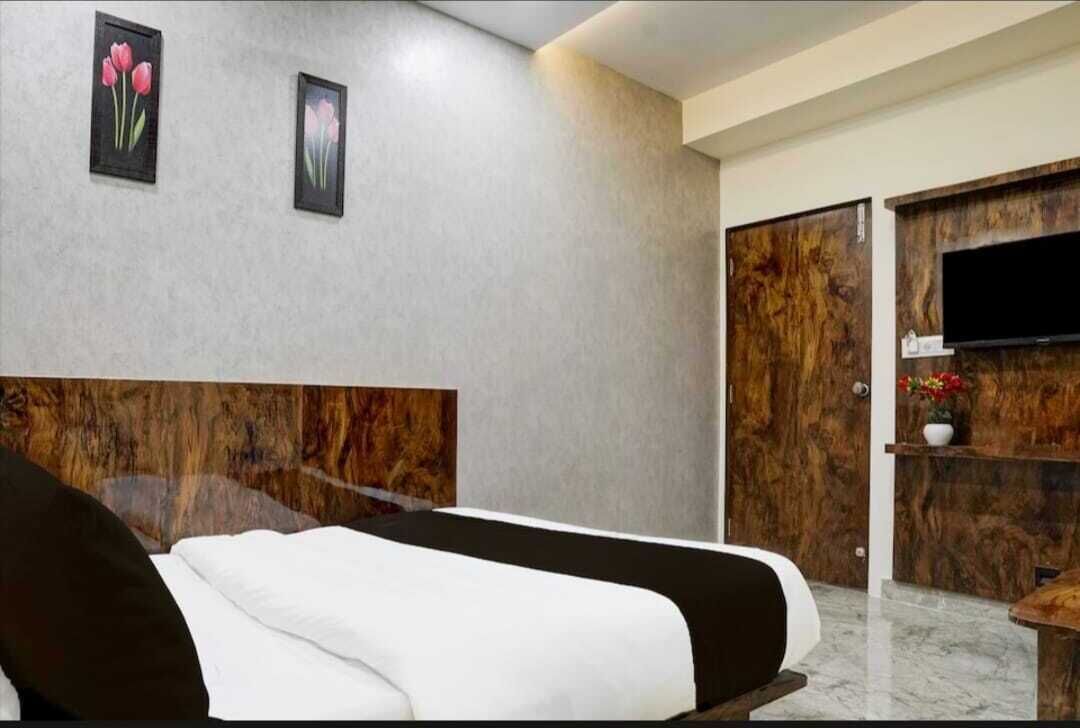 A modern hotel room with a large bed, a wooden headboard, a flat-screen TV, and a wooden wardrobe.