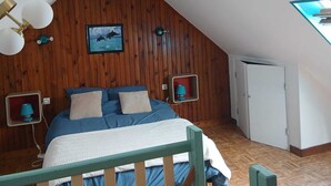 A bedroom with a sloped ceiling, wooden paneling, a bed with blue bedding, two wall-mounted lamps, a framed picture, and a white door. - 2-person house with sea view 600 meters from the beach (PLOMODIERN)