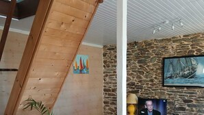A living room with a blue sofa, a wooden staircase, a stone wall, and a television. - 2-person house with sea view 600 meters from the beach (PLOMODIERN)