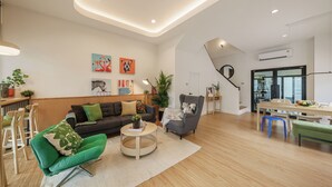 Un salon moderne comprenant un canapé, un fauteuil et une table basse, un coin repas avec une table et des chaises, et un escalier menant à un autre niveau.