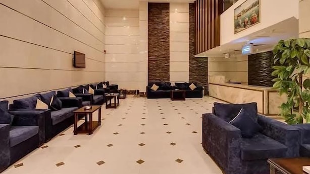 A spacious lobby with multiple dark blue sofas arranged in rows, a central column with a textured wall, and a reception desk with a plant. - Al Naseem Hotel (Makkah)