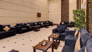 A spacious lobby with rows of dark blue sofas and armchairs, a large potted plant, and a stone accent wall. - Al Naseem Hotel (Makkah)