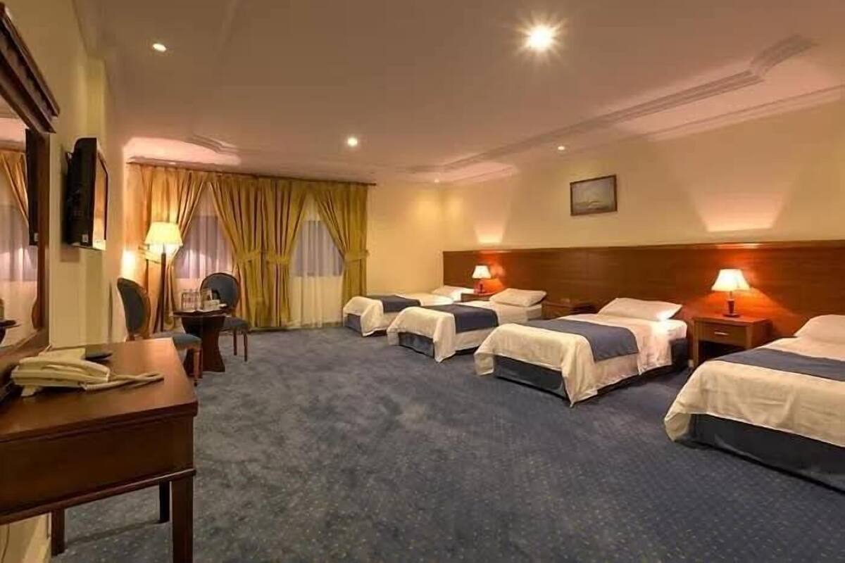 A hotel room with four single beds, a desk, a chair, and a lamp.