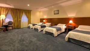 A hotel room with four single beds, a small table with a chair, and a window with curtains. - Al Naseem Hotel (Makkah)