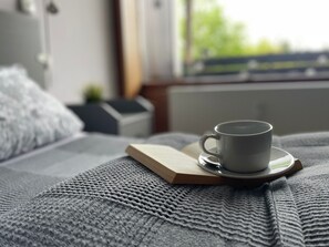 A cup of coffee on a coaster with a book on a bed. - Vacation Apartment in Freudenstadt-Kniebis II, Black Forest (Freudenstadt)