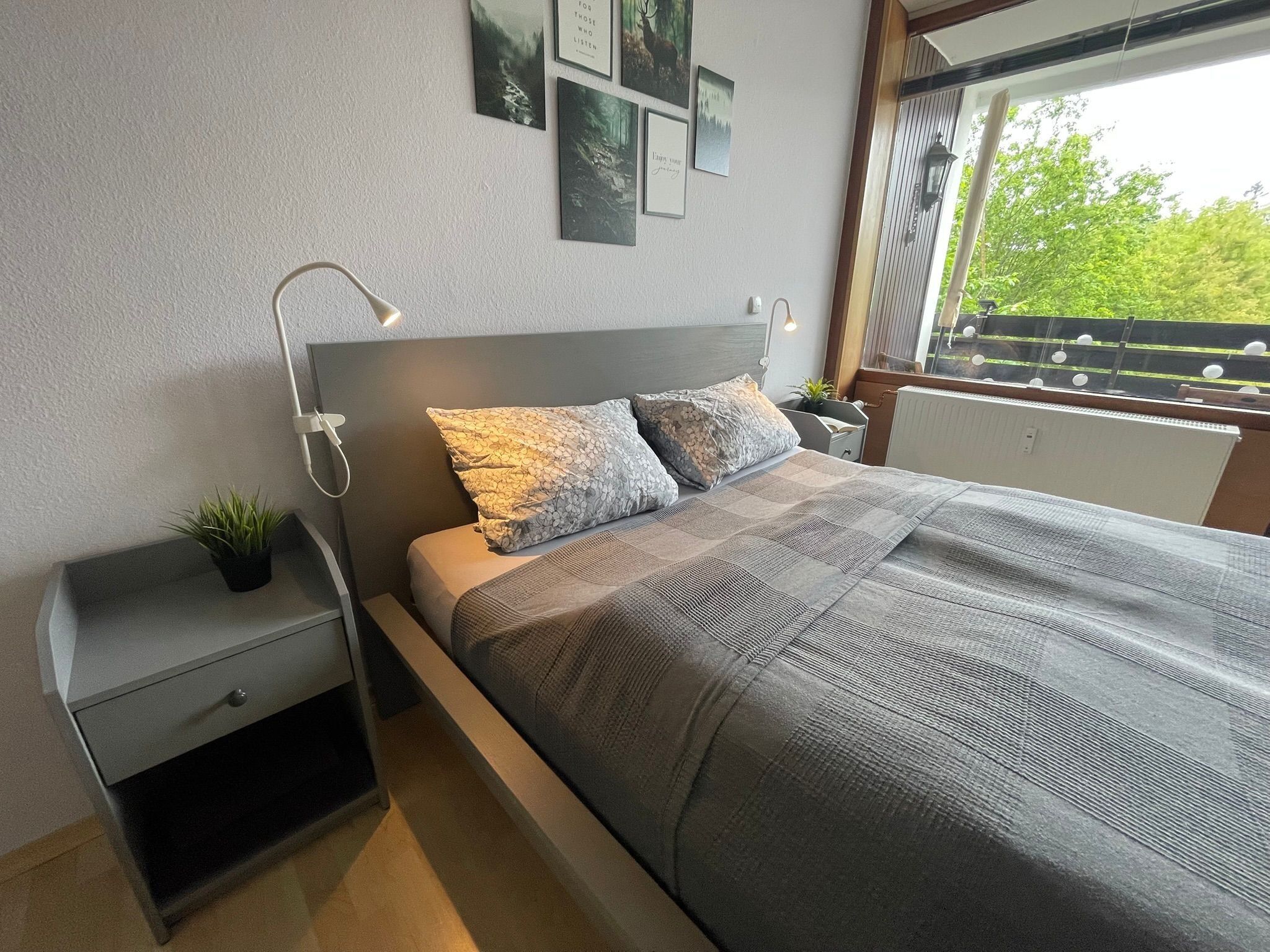 A modern bedroom with a bed, bedside tables, a small plant, and framed pictures on the wall.
