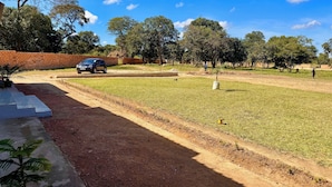 A paved pathway leading to a grassy area with a brick wall and trees in the background. - The Ridge Grandstay (Manyama)