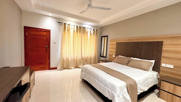 A bedroom with a bed, a wooden headboard, a ceiling fan, and a door. - The Ridge Grandstay (Manyama)