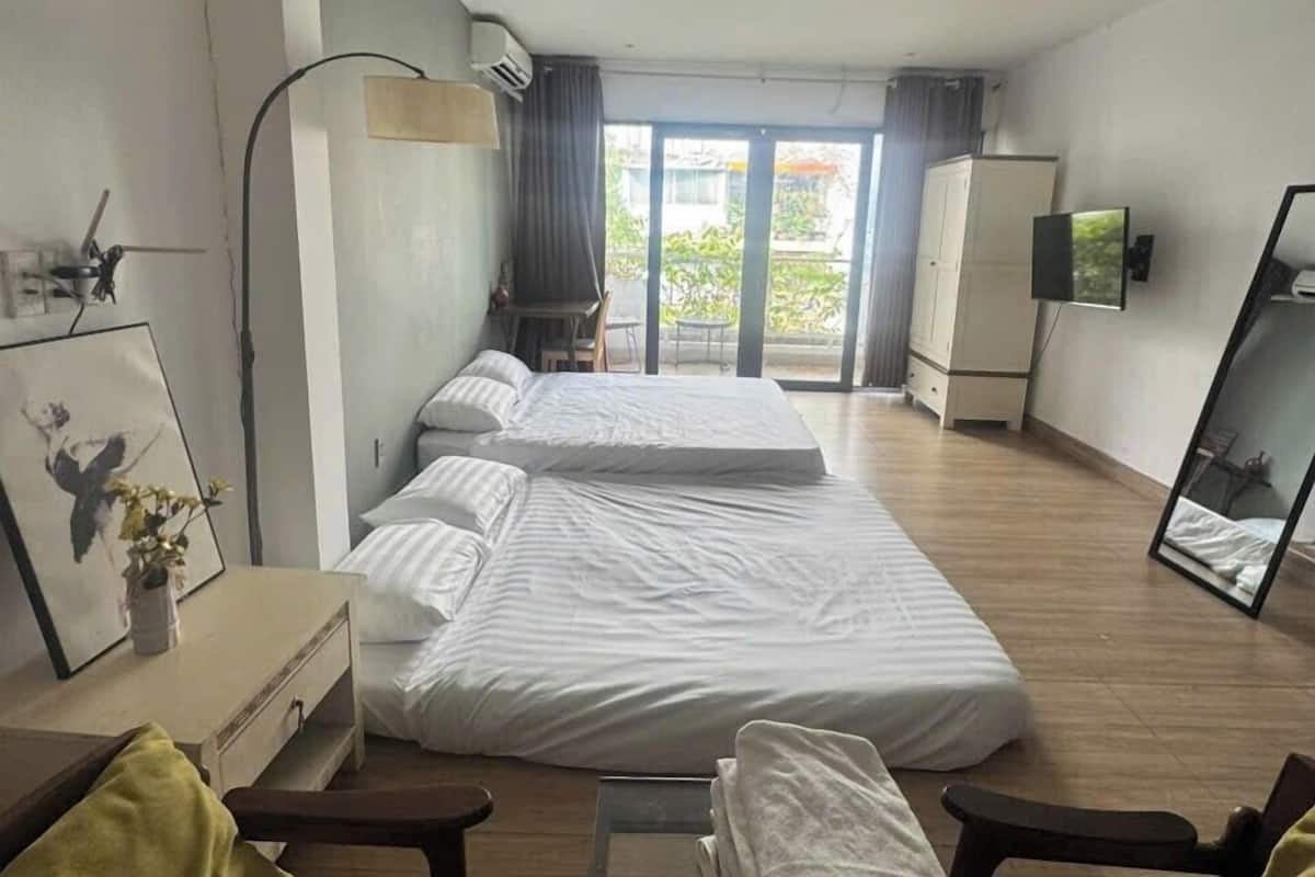A hotel room with two beds, a desk, a chair, a TV, and a balcony with a view.
