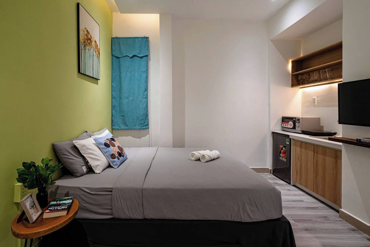 A compact hotel room with a bed, bedside table, TV, and a small kitchenette.