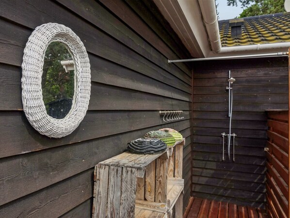 Un mur extérieur en bois agrémenté d’un miroir à motifs tissés, un petit banc en bois et un espace douche.