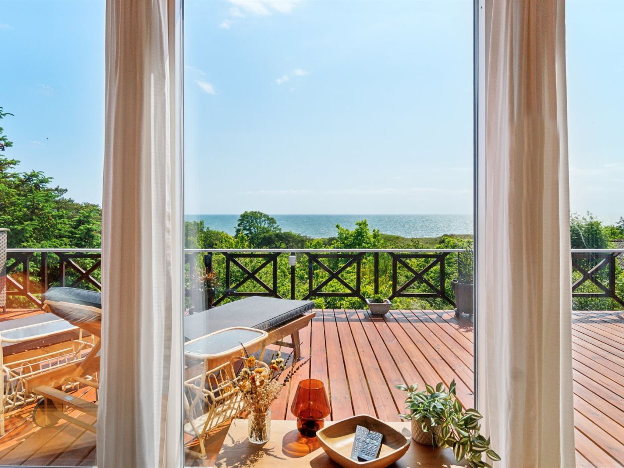 Eine Holzterrasse mit Meerblick, ein Tisch mit Stühlen und einem Geländer.