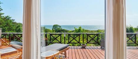 Eine Holzterrasse mit Meerblick, ein Tisch mit Stühlen und einem Geländer.