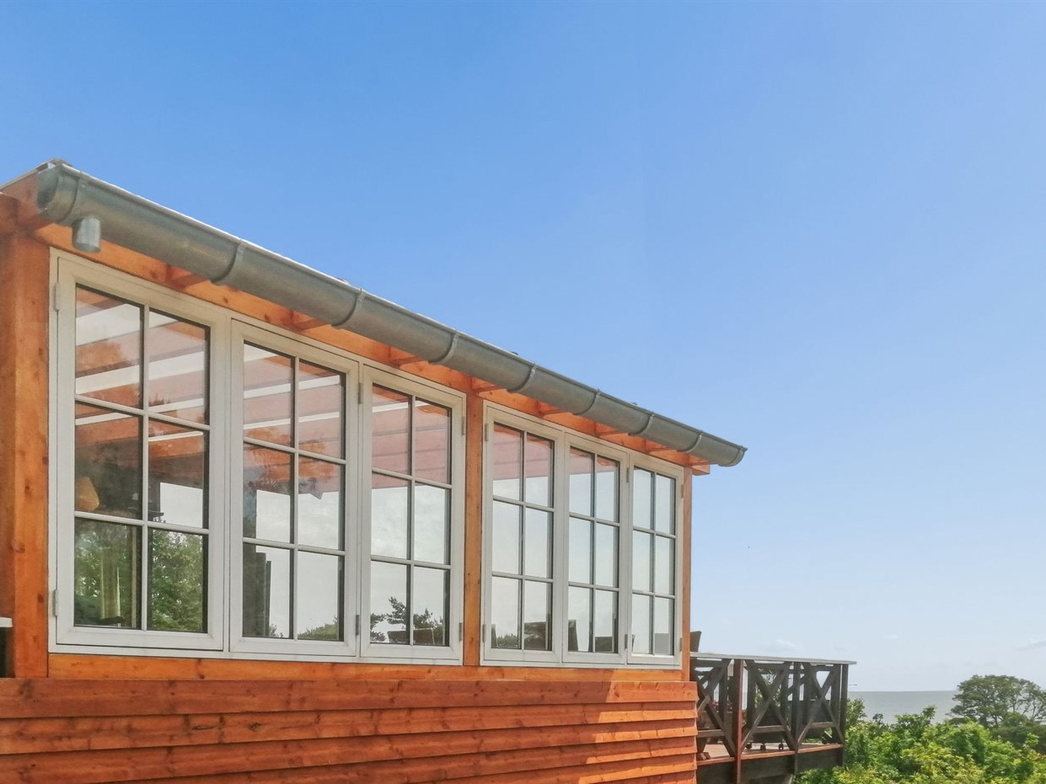 A wooden cabin with large windows and a balcony overlooking a body of water.