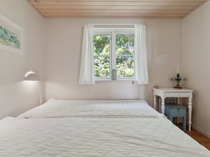 Une chambre avec deux lits, une fenêtre avec des rideaux blancs, une lampe de chevet et une petite table avec une lampe.