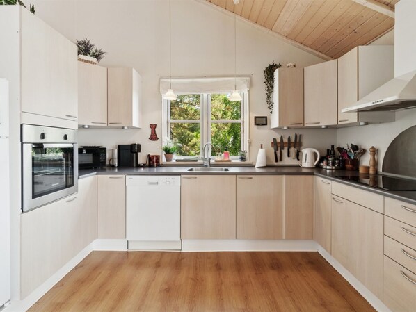 Eine moderne Küche mit Holzschränken, Backofen, Geschirrspüler und einem Fenster für natürliches Licht.