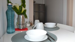 A dining table with white plates, a blue water bottle, a silver pitcher, and a white vase with green leaves. - Avio Apartament - Pedrouso View Suite (Santiago de Compostela)
