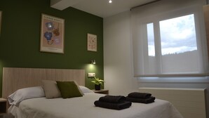 A hotel room with a bed, a nightstand with a plant, a window with a view, and a wall with a flower market poster. - Avio Apartament - Pedrouso View Suite (Santiago de Compostela)