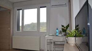 A room with a white desk, a chair, a radiator, a window with a view, and a potted plant. - Avio Apartament - Pedrouso View Suite (Santiago de Compostela)