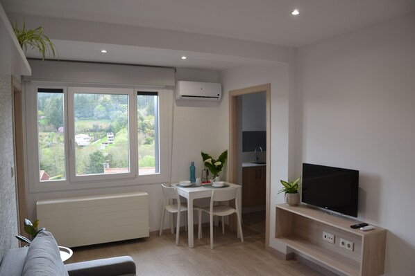 A modern living room with a dining area, a TV, and a view of the outdoors.