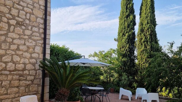 A patio area with stone walls, a brick floor, outdoor furniture, and tall trees.