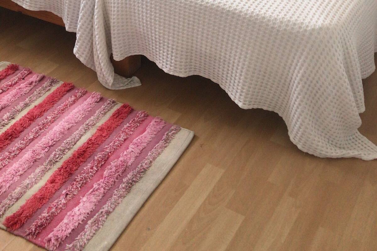 Una cama doble con ropa de cama blanca y dos almohadas, un cabecero de madera, una mesita de noche con una lámpara y un cuadro floral enmarcado en la pared.