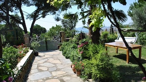 A stone pathway leading to a wooden table and chairs, surrounded by lush greenery and potted plants. - Günebakan Taliani Otel (Ayvalik)