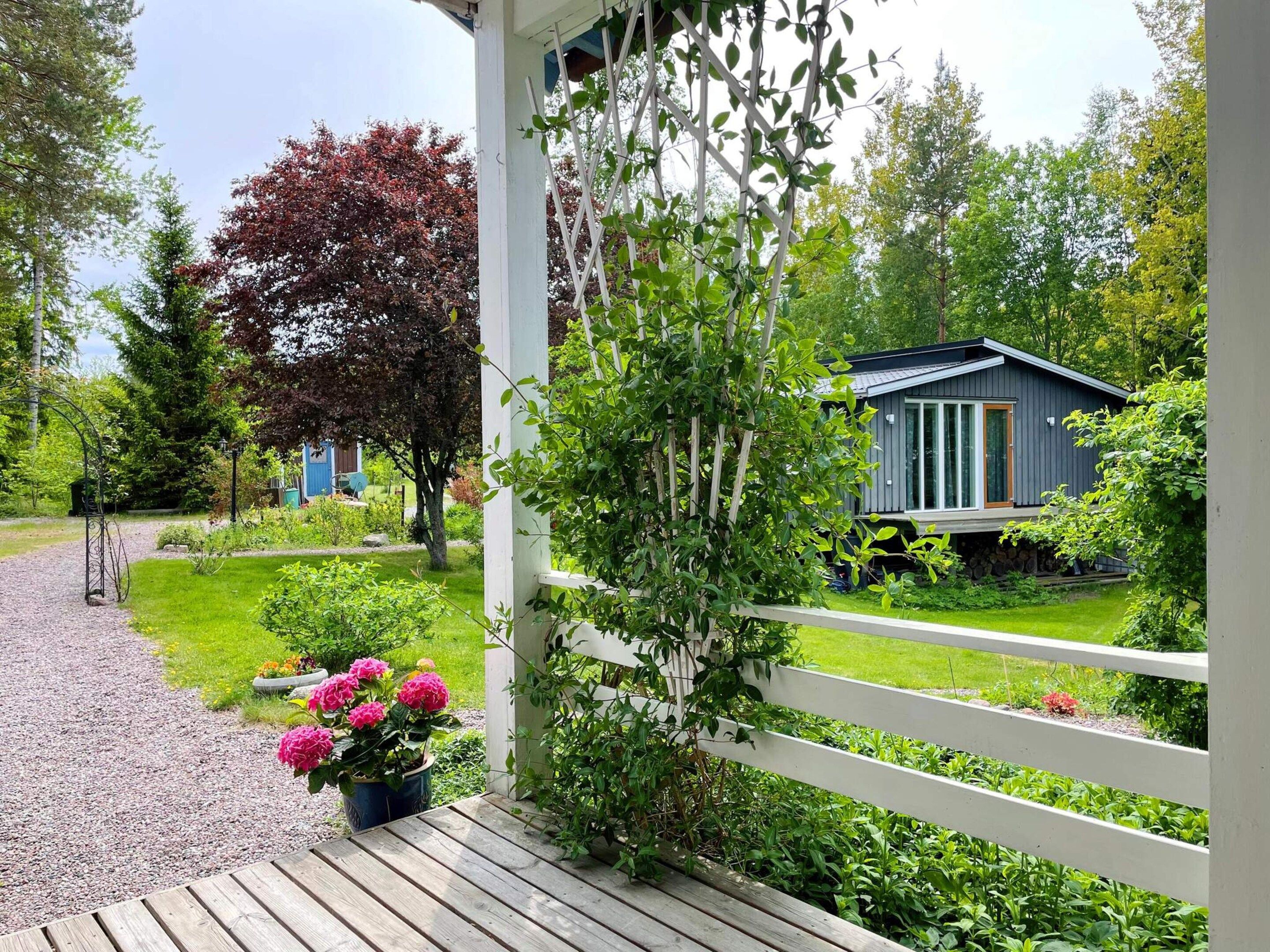 Um deck de madeira com cerca branca, um jardim com flores e uma casa com fachada azul.