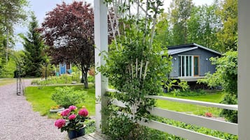 Um deck de madeira com cerca branca, um jardim com flores e uma casa com fachada azul.