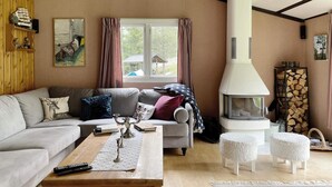 Ein gemütliches Wohnzimmer mit Kamin, einer Couch, einem Couchtisch und einem fenster mit Vorhängen.