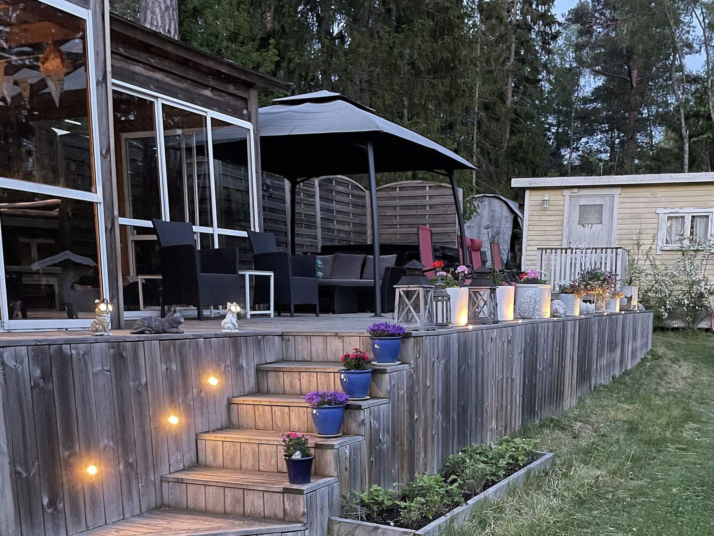 A wooden deck with outdoor furniture, potted plants, and a staircase leading to a covered area.