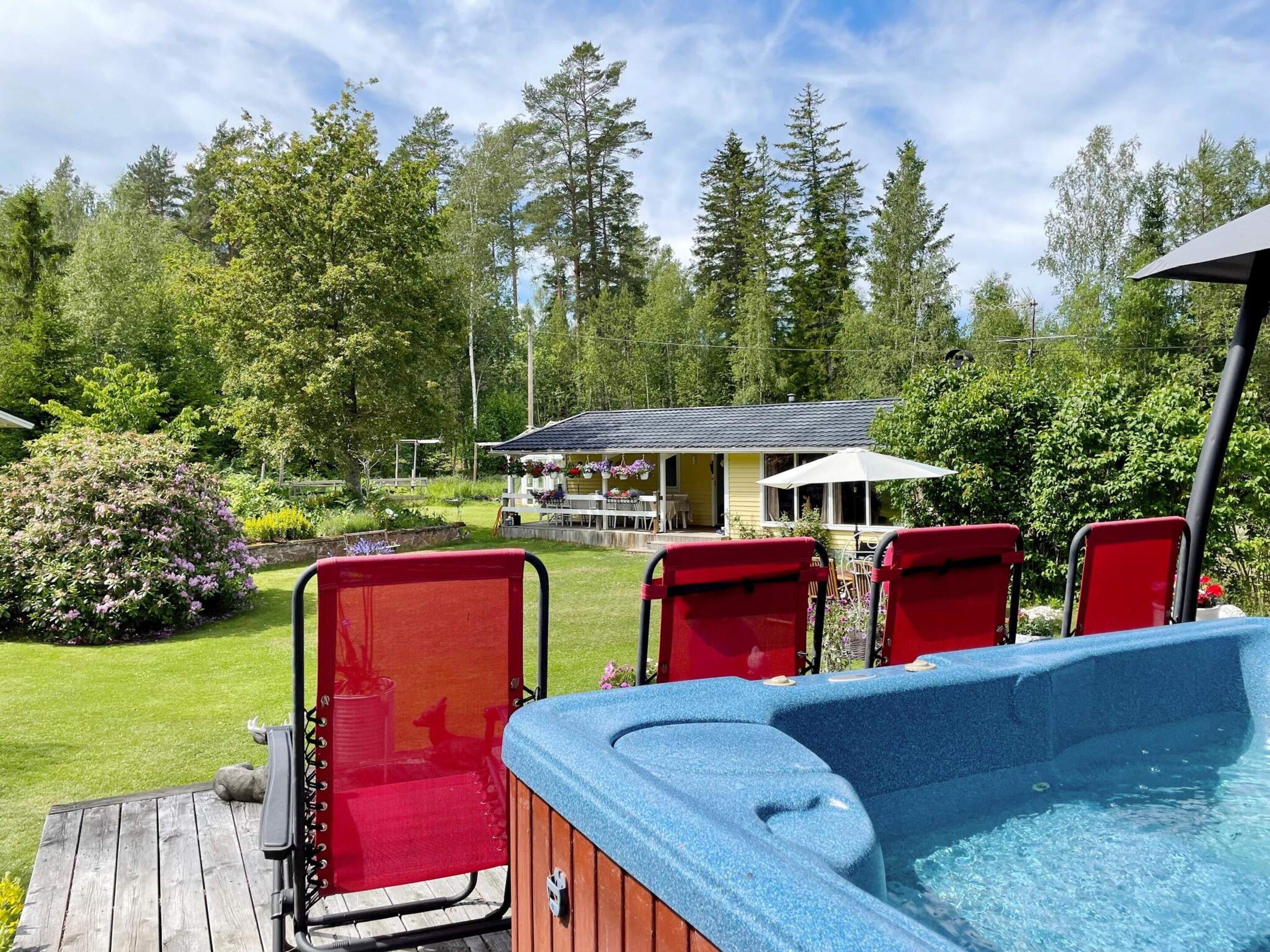 Un jacuzzi con sillas rojas, una terraza de madera y una casa al fondo.