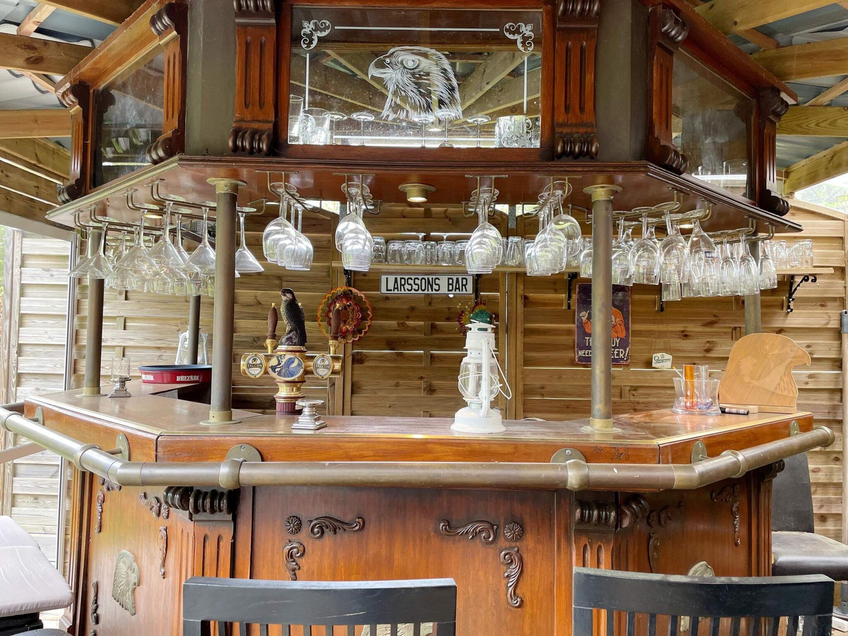 A wooden bar with a sign reading 'LARSSONS BAR,' featuring a decorative eagle and various glassware.