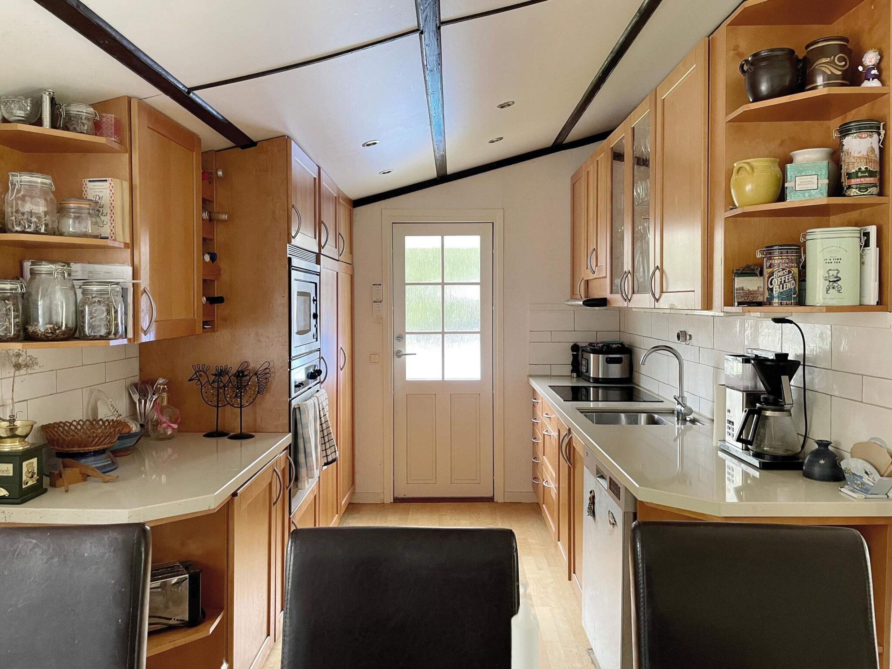 Una cocina con armarios de madera, microondas, cafetera y varios frascos en estantes.