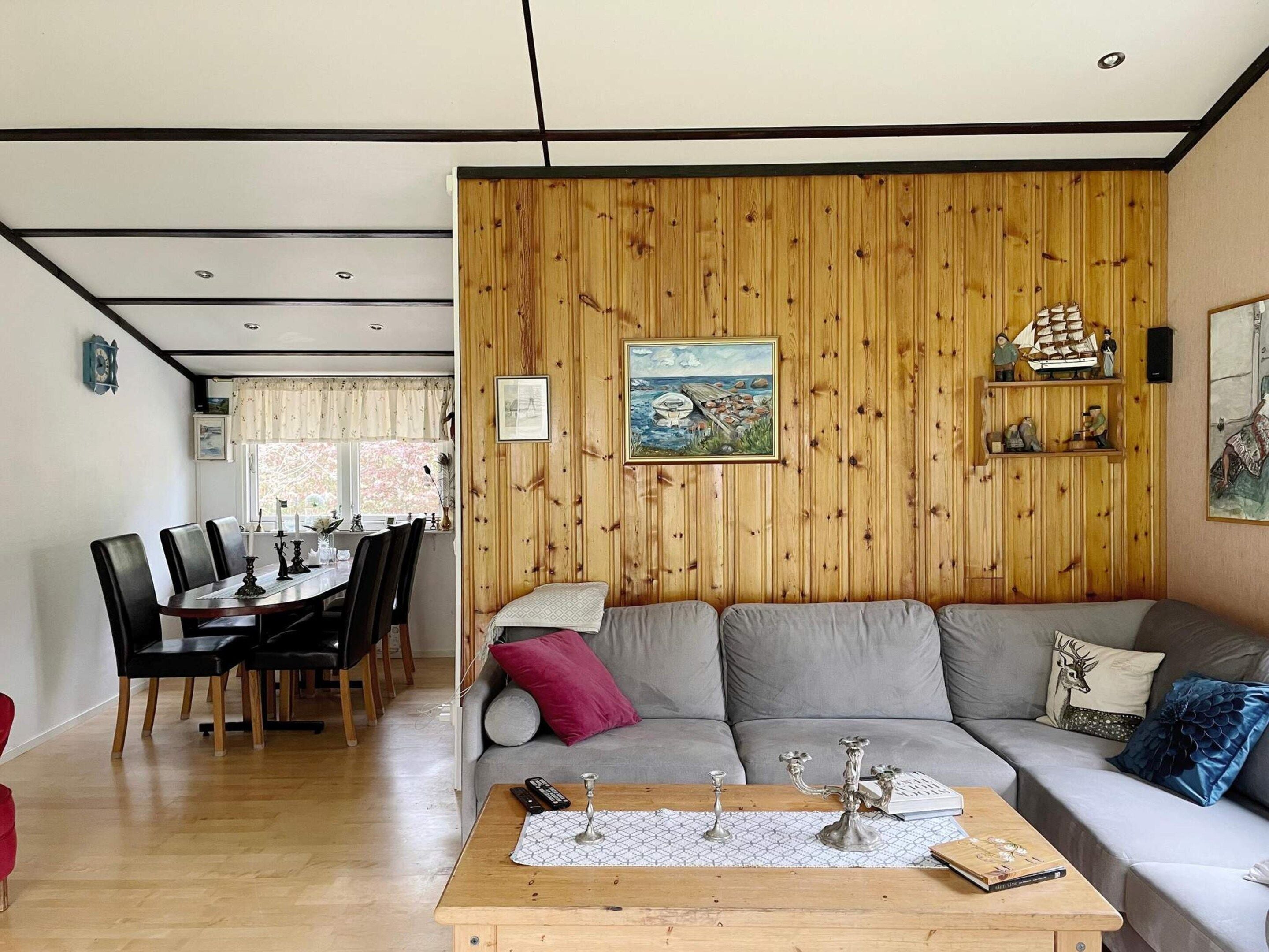 A living room with a wooden wall, a sofa, a coffee table, and a dining area with chairs and a table.