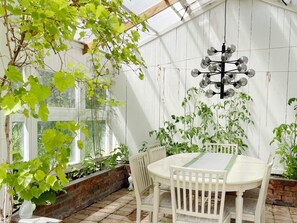 A conservatory with a round table and chairs, surrounded by potted plants and a hanging light fixture. - 5 Star Holiday Home in Graddo (Gräddö)