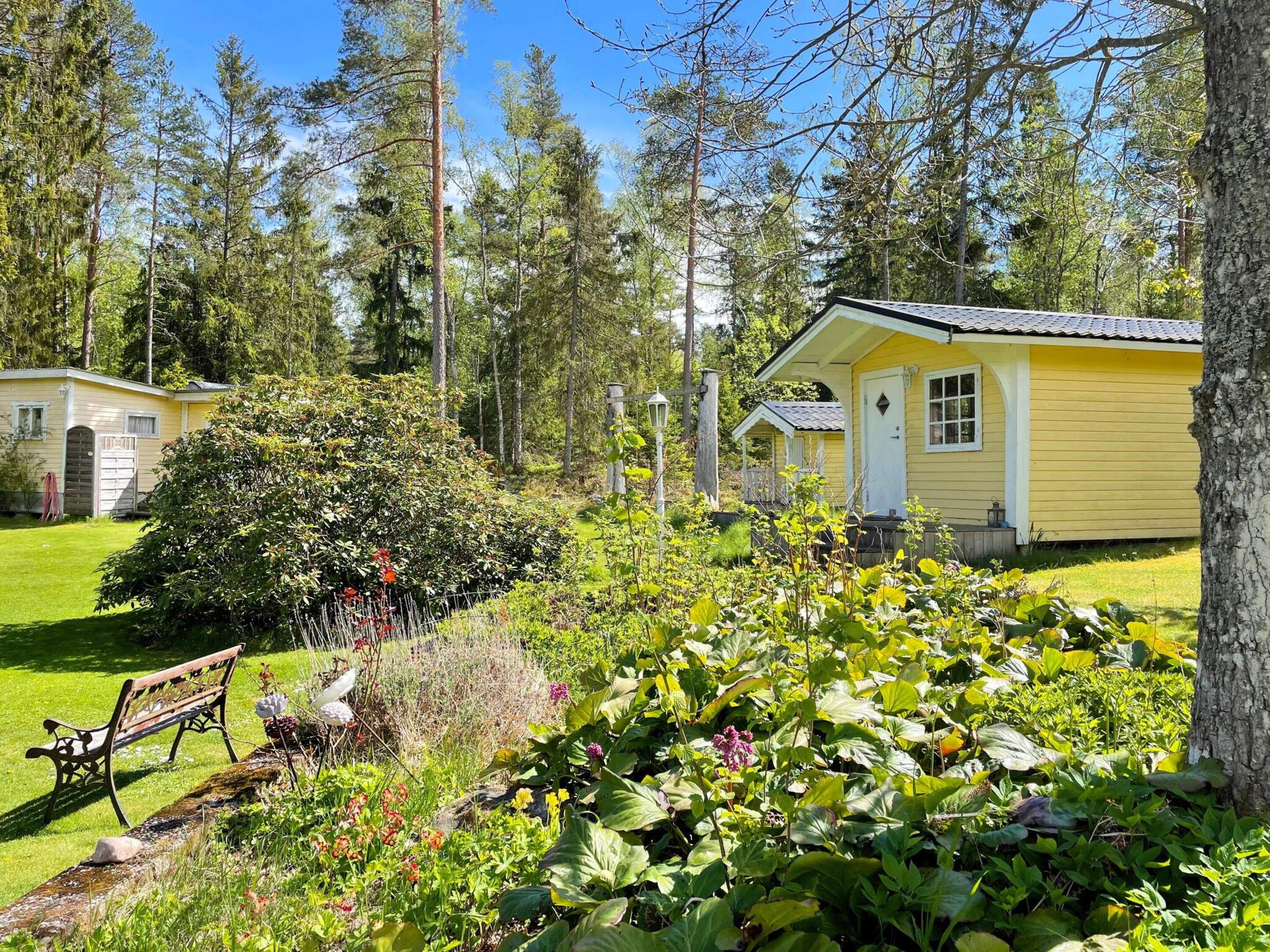 A yellow cabin with a small porch, surrounded by lush greenery and tall trees.