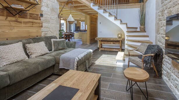 A spacious living area with a wooden staircase, a sofa, a coffee table, and a dining table. - 🏡 La Cabane à Camillo – Warm and Cozy Retreat (CHEVALINE)